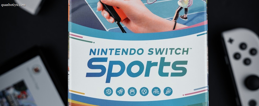 A box of Nintendo Switch Sports is prominently featured, surrounded by various Nintendo Switch controllers and a screen displaying a related interface. The box art depicts animated characters playing sports, such as tennis, with vibrant colors and action-oriented poses.
